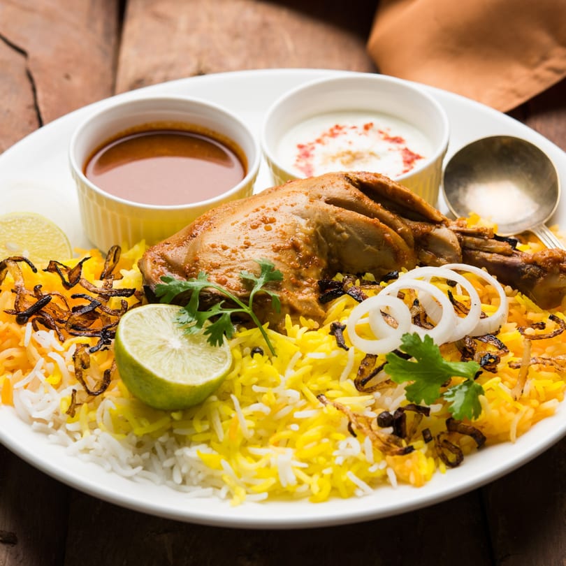 Mahek's chicken biryani with yellow and white rice, fried onions, lime, and two sauces.